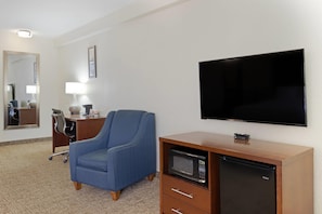 Habitación de hotel con televisión de pantalla plana, microondas, sillón azul, escritorio con lámpara y espejo.