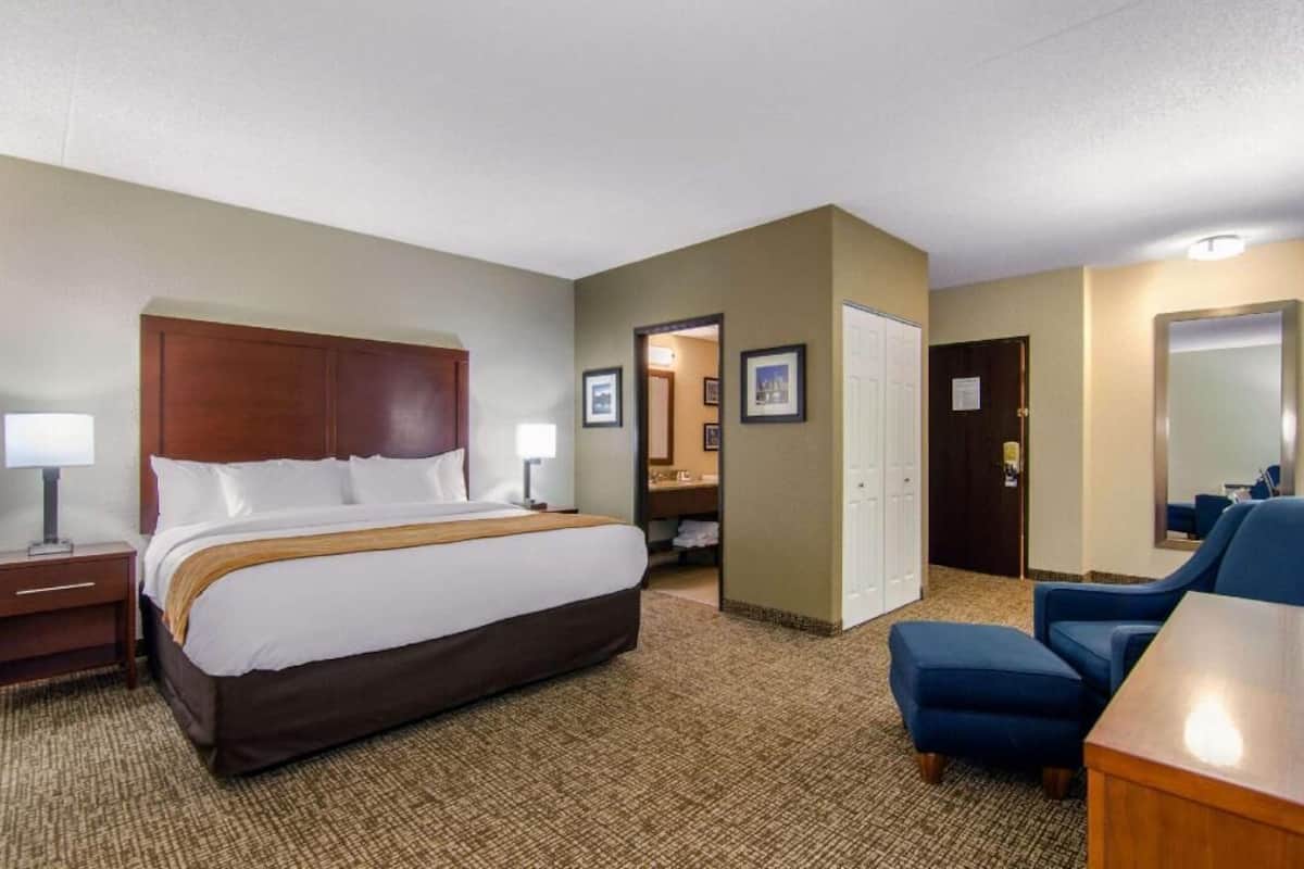 A hotel room with a bed, a desk, a chair, and a bathroom visible through an open door.