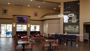 A spacious indoor area with multiple tables and chairs, large windows, and a high ceiling with hanging lights. - Comfort Inn & Suites Wichita Northeast (Wichita)