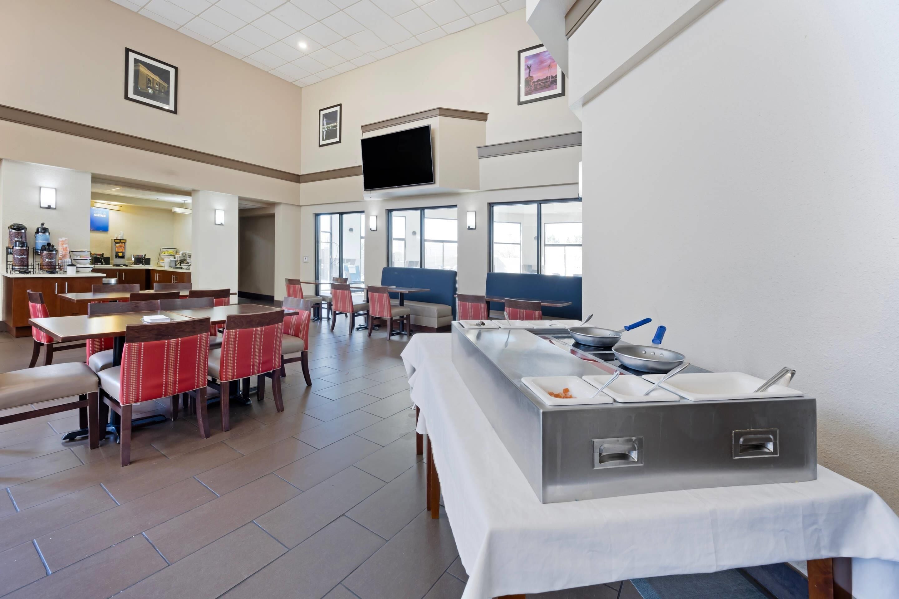 Une salle à manger d’hôtel avec des tables, des chaises, un buffet et un téléviseur fixé au mur.