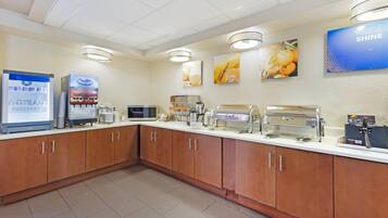 A breakfast area with a refrigerator, coffee machines, and a buffet setup.