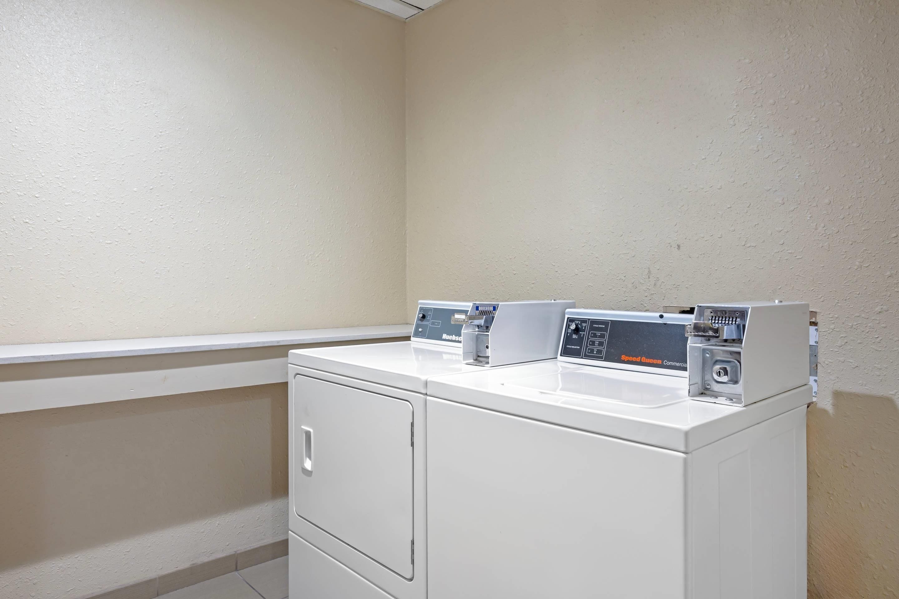 Un espace buanderie comprenant un lave-linge et un sèche-linge blancs, un petit meuble de rangement et un panneau de commande fixé au mur.