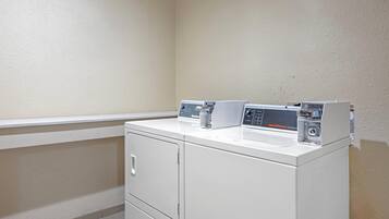 Un espace buanderie comprenant un lave-linge et un sèche-linge blancs, un petit meuble de rangement et un panneau de commande fixé au mur.