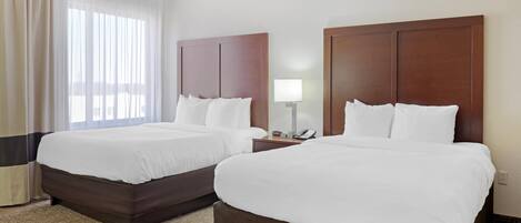 A hotel room with two beds, a nightstand with a lamp, and a window with curtains.