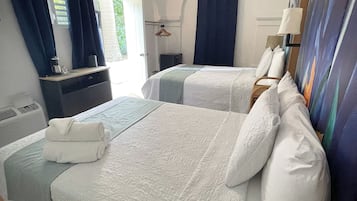 Habitación de hotel con dos camas, ventilador de techo, un cuadro en la pared y ventana con cortinas.