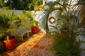 Um pátio com piso de azulejos, plantas em vasos e uma parede branca com um emblema decorativo.