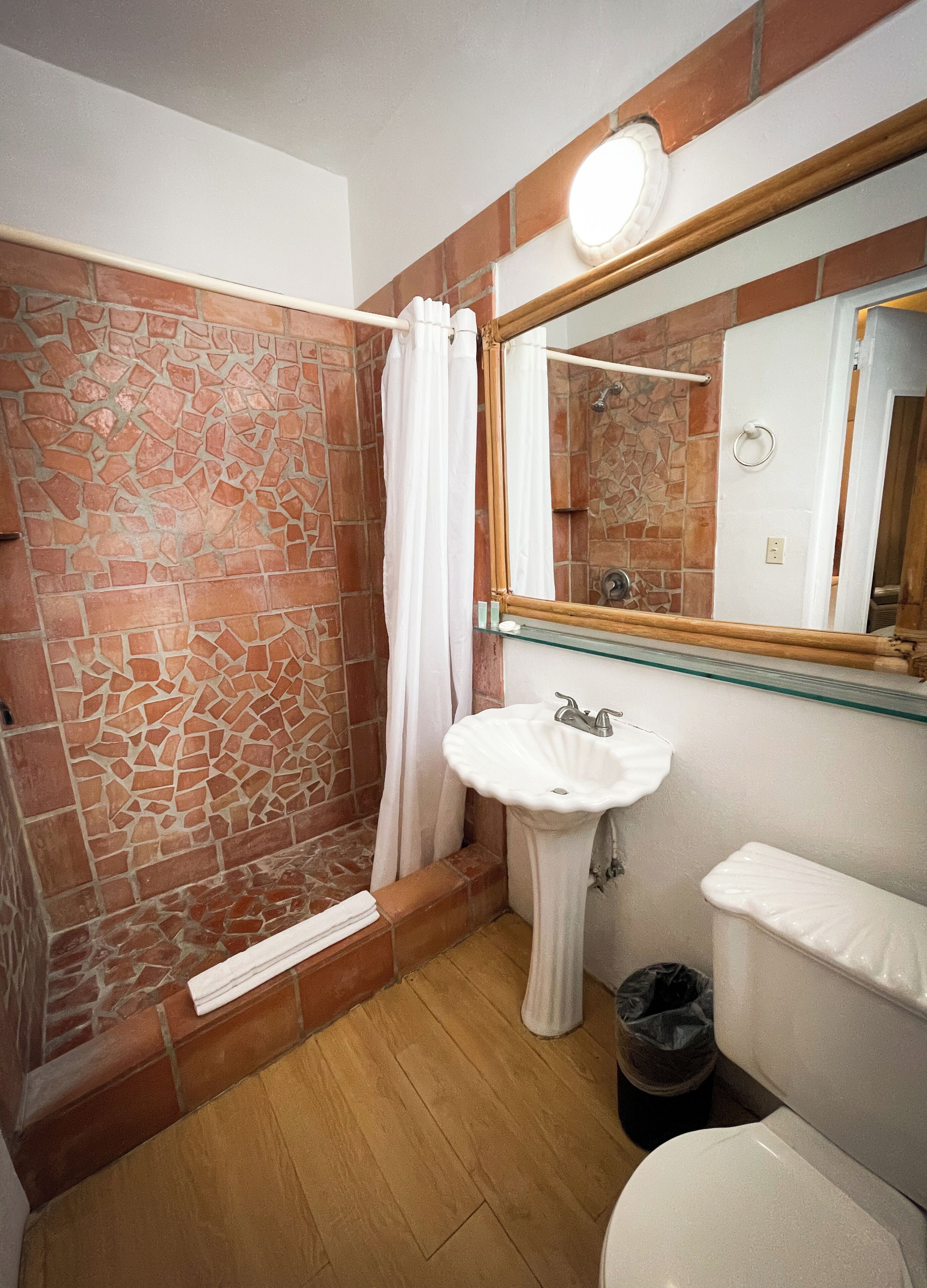 Une salle de bain avec un mur de douche en pierre, un lavabo blanc, un miroir et des toilettes.