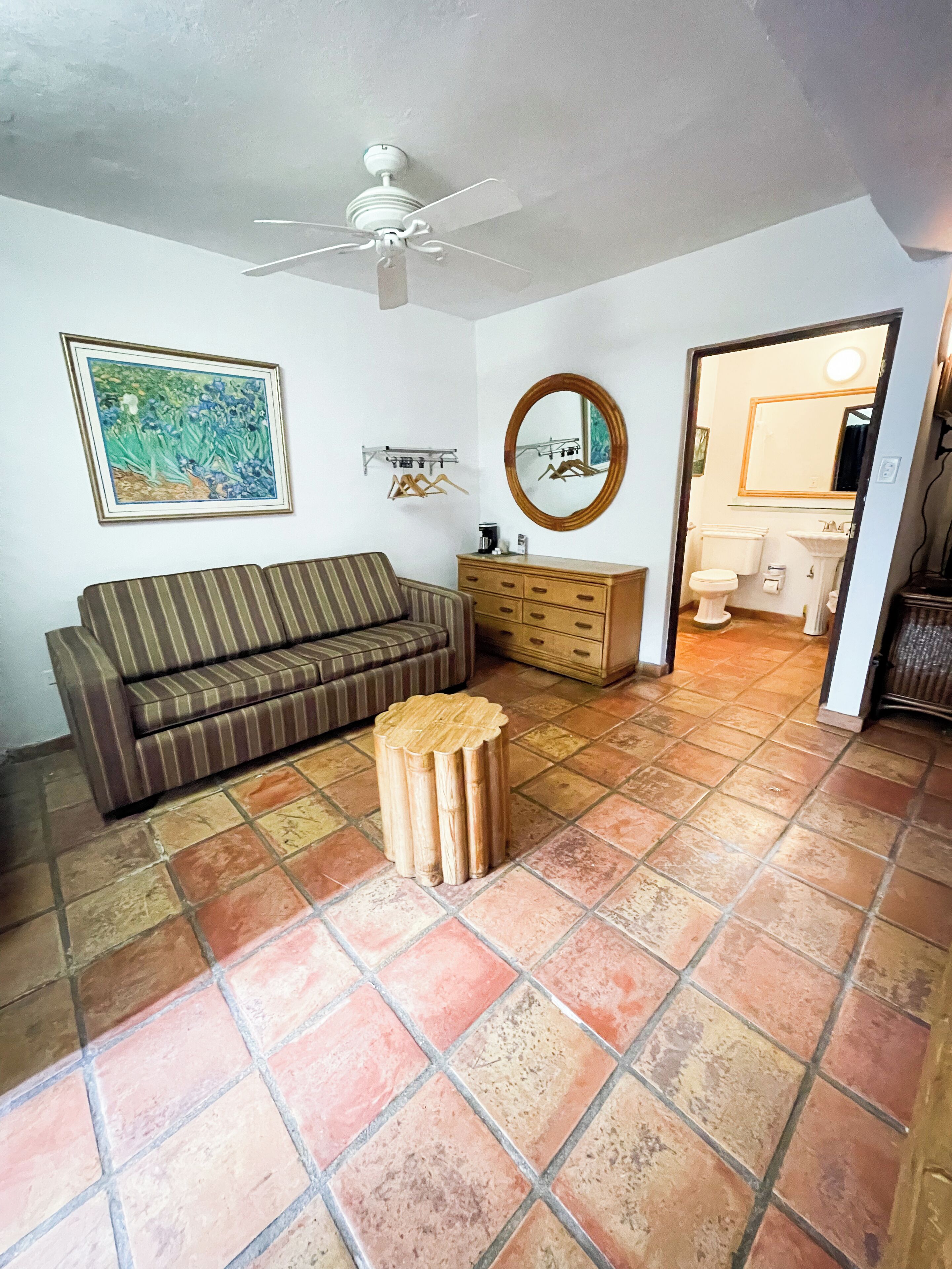 Una sala de estar con un sofá a rayas, un mueble de madera, un espejo redondo y un ventilador de techo.