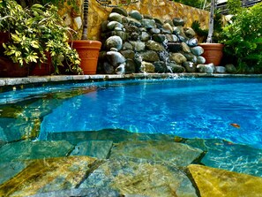 Ein klares Schwimmbecken, umgeben von Felsen und Kübelpflanzen.