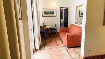 A hallway with a tiled floor, a dining area with a table and chairs, and a sofa.