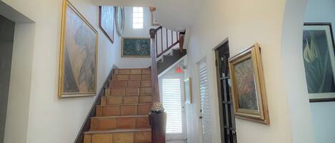 A staircase with a wooden handrail, leading to a landing with a chandelier.