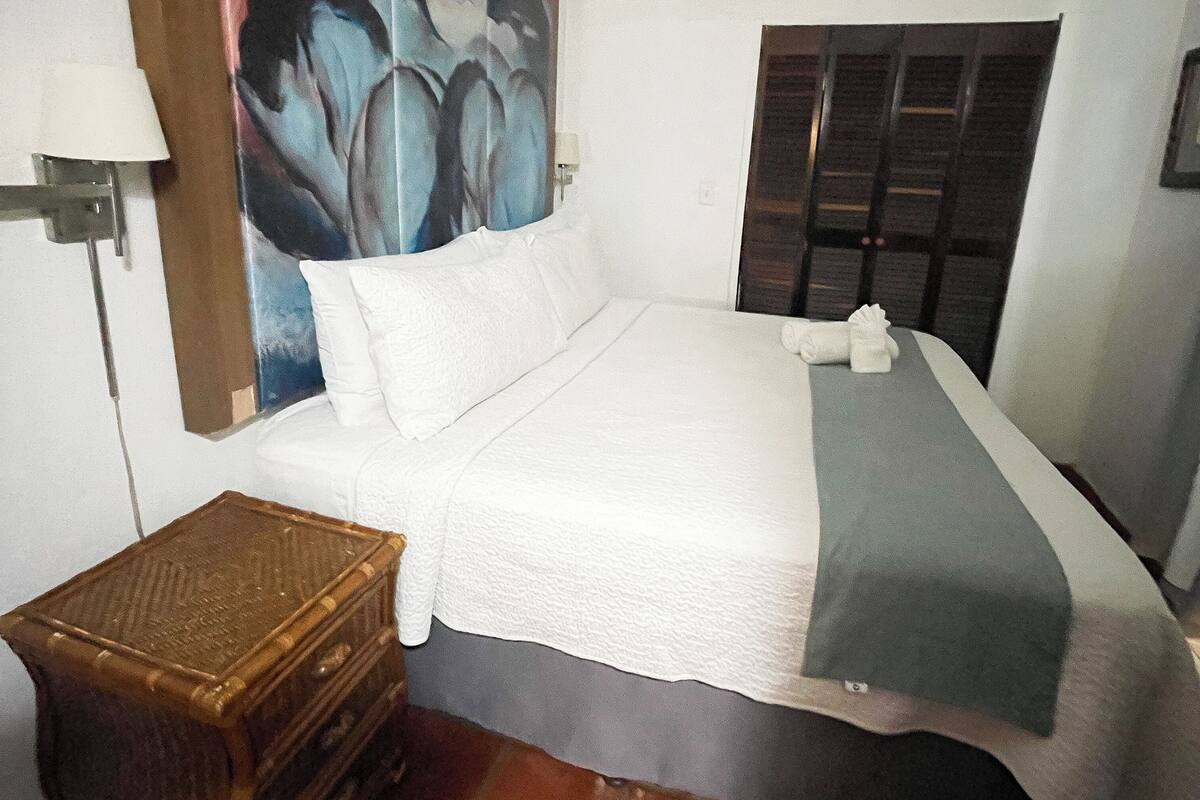 A hotel room with a bed, a painting, a window, and a nightstand.