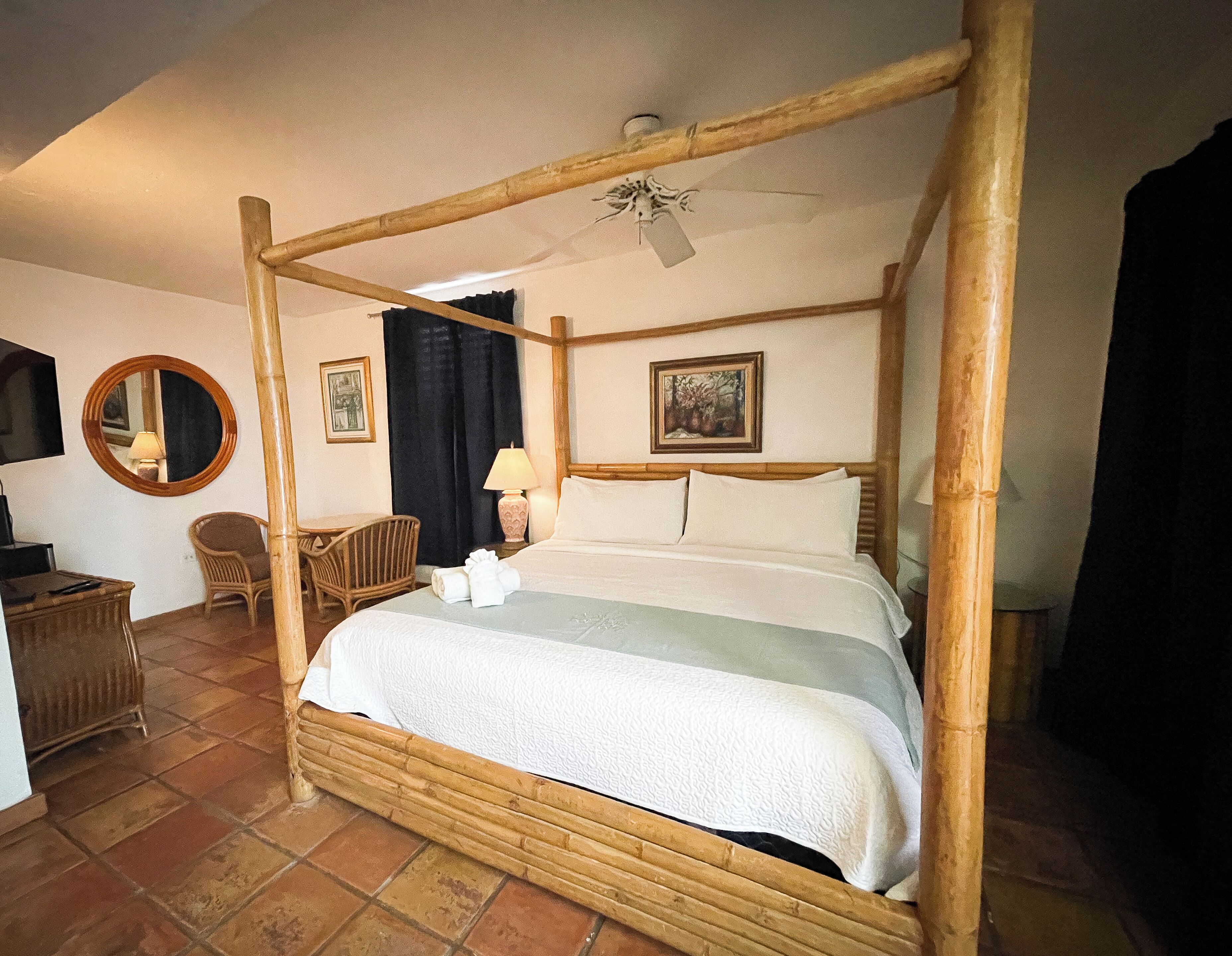 Un lit à baldaquin avec un ventilateur de plafond, une chaise, un bureau et un miroir.