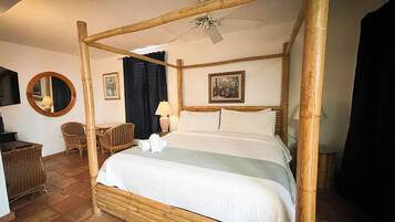 A four-poster bed with a ceiling fan, a chair, a desk, and a mirror.
