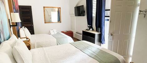 A hotel room with two beds, a ceiling fan, a TV, a mirror, and a door.