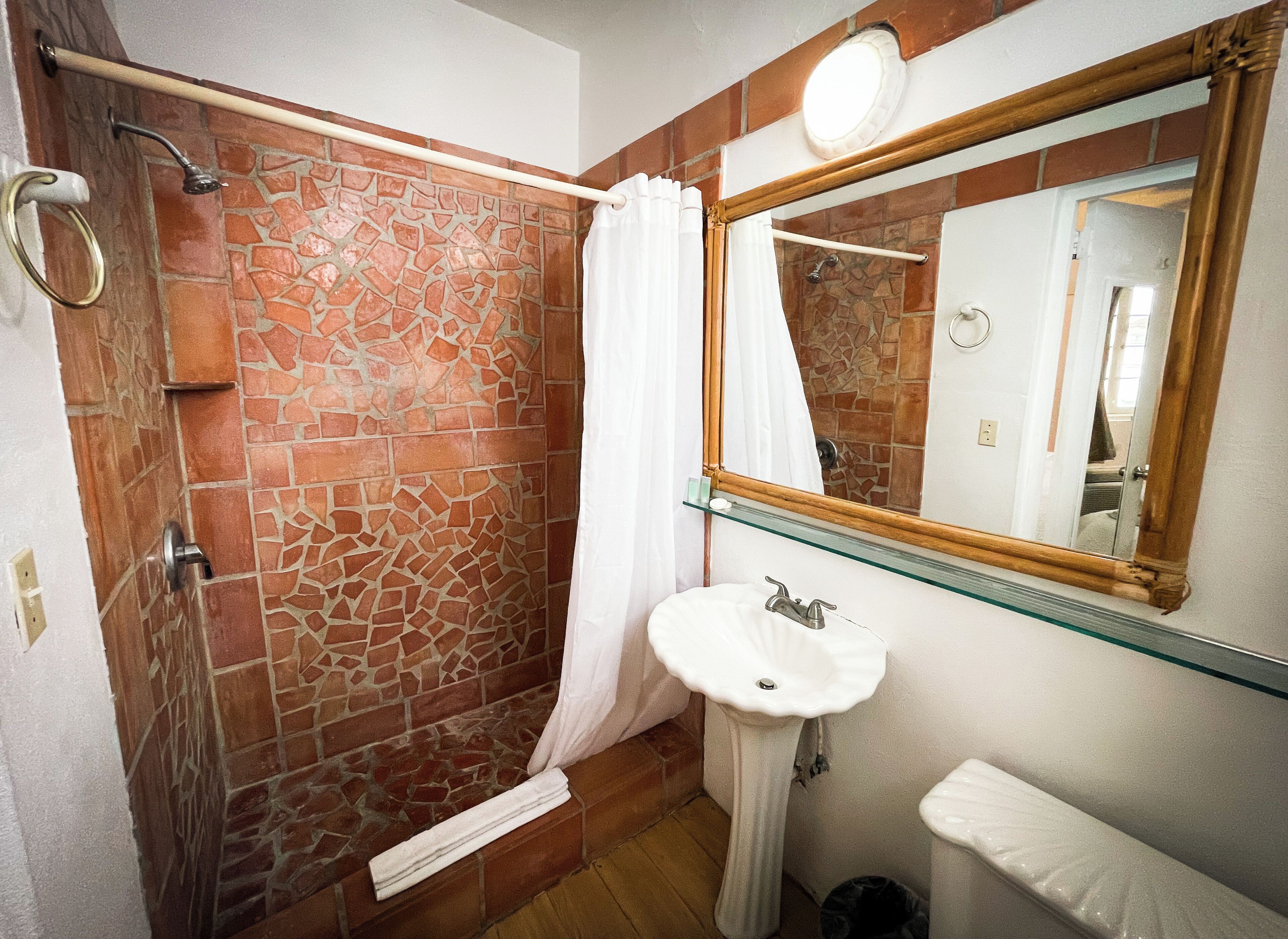 Un baño con ducha de piedra, un estante de vidrio sobre el lavamanos y un espejo grande.