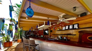 Un área de bar con mostrador, sillas, ventiladores de techo y plantas en macetas.