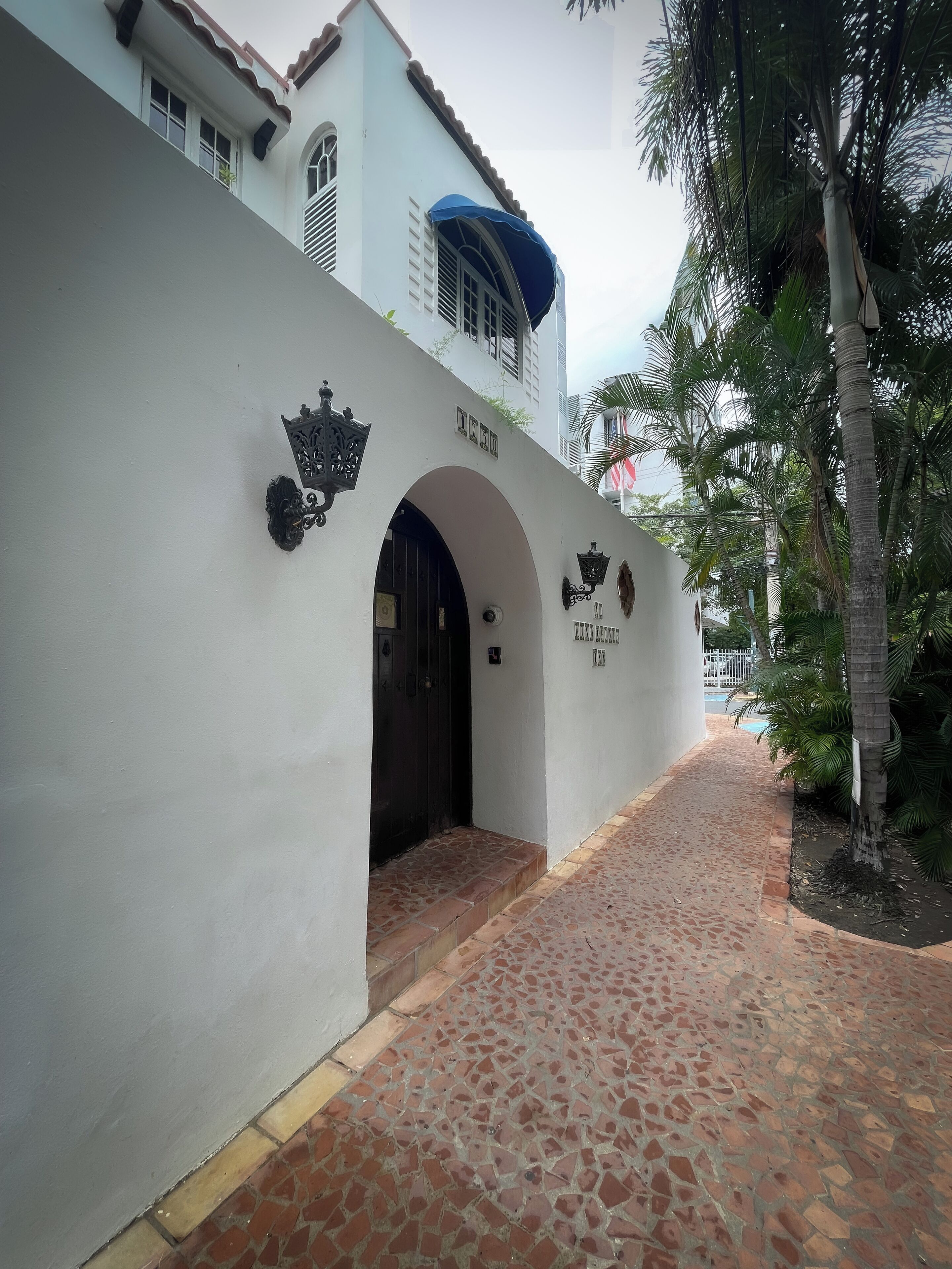 A building entrance with a tiled pathway leading to a dark entrance door, surrounded by white walls and decorative elements.