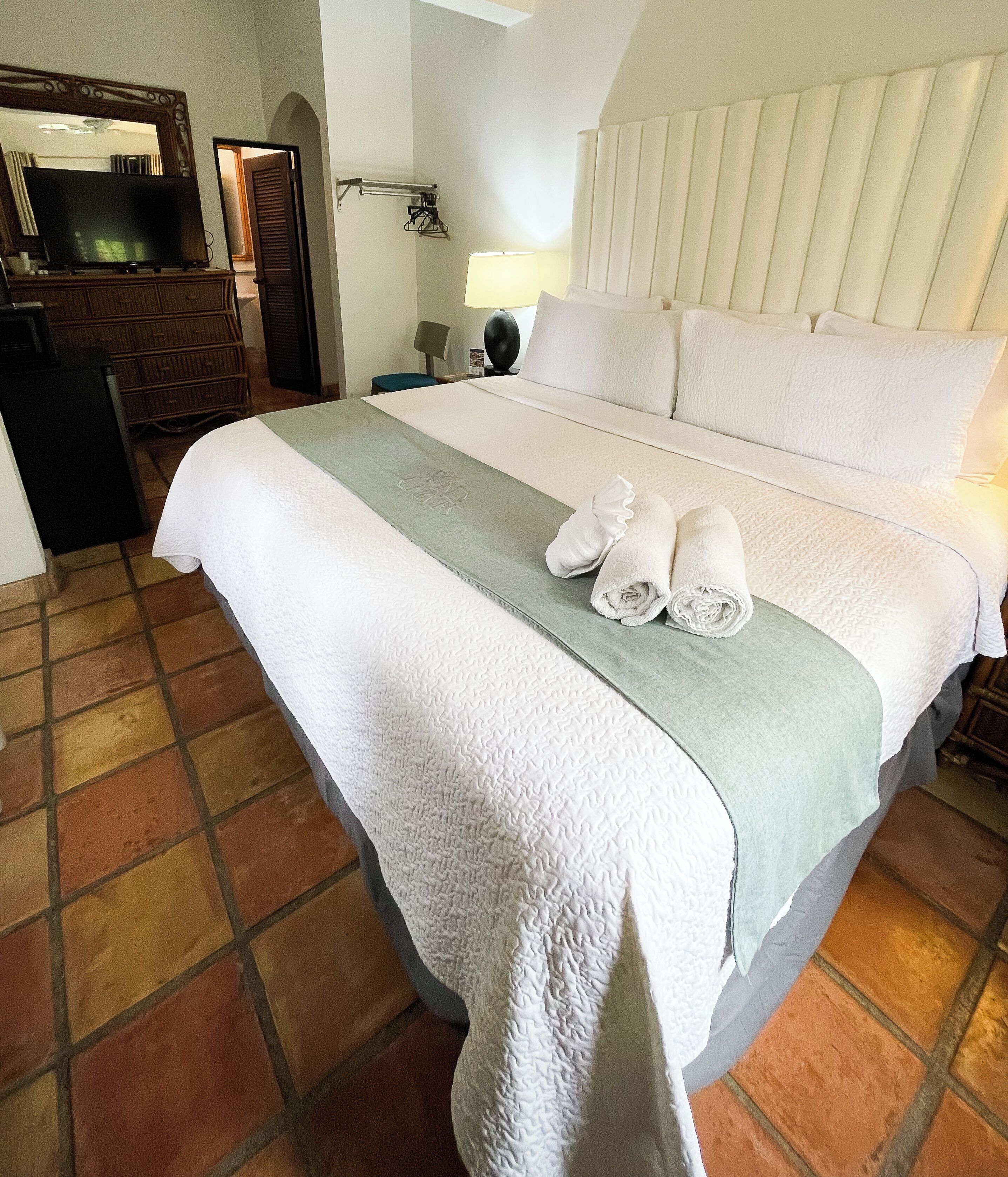 A neatly made bed with a white comforter and a green towel.