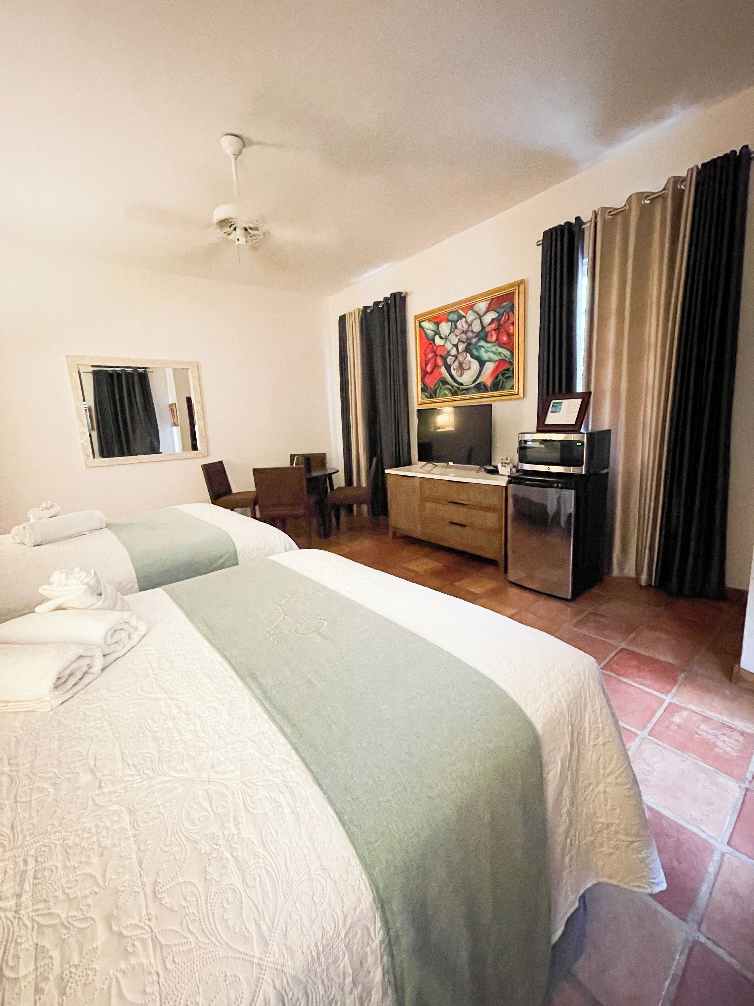 Ein Hotelzimmer mit zwei Betten, einem Schreibtisch mit Computer, einem Fernseher und einem Gemälde an der Wand.