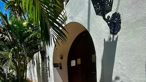 Un patio con suelo de baldosas, una puerta de madera y una pared blanca con un adorno decorativo.