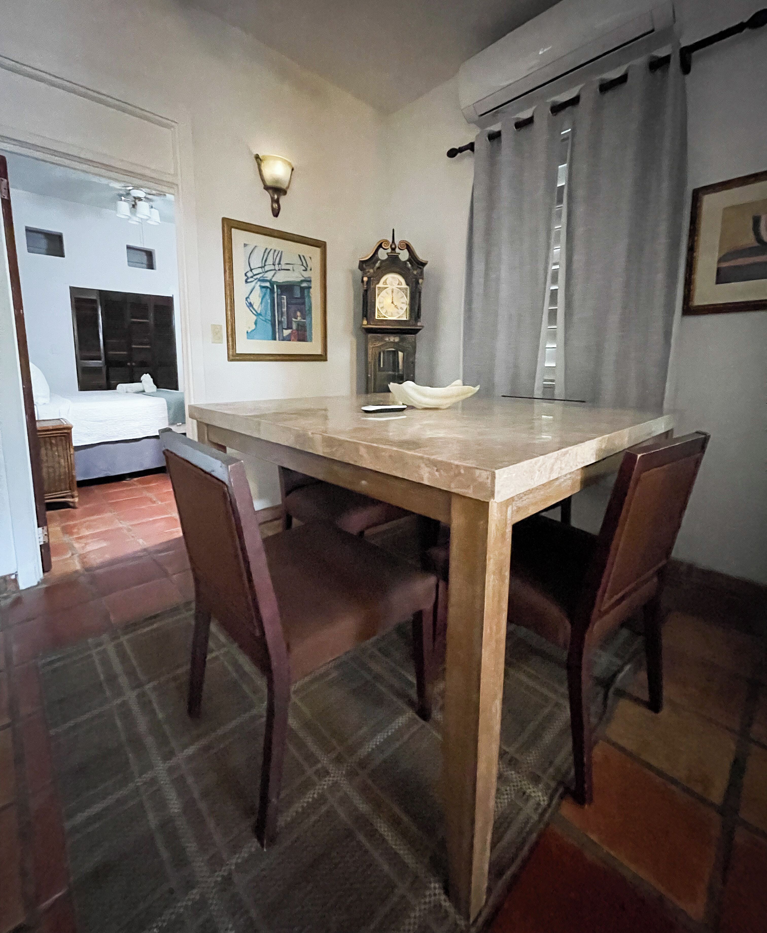 Un comedor con una mesa de madera, dos sillas, un reloj y una lámpara fijada a la pared.