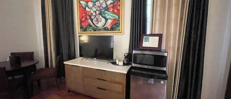 A compact hotel room with a kitchenette, a dining table, and a large floral artwork on the wall.
