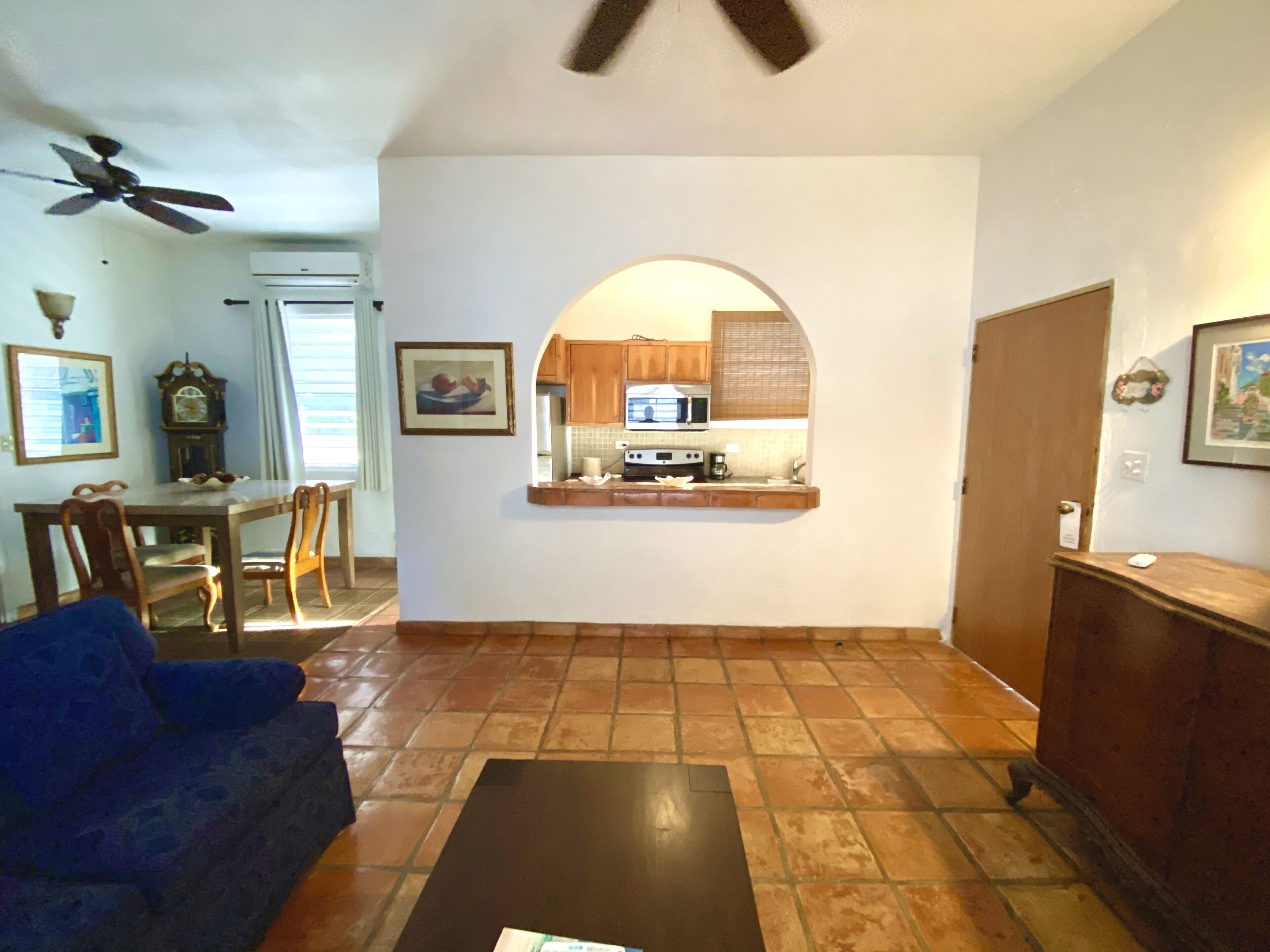 Una sala de estar con un sofá azul, una mesa de centro y vista hacia la cocina a través de un arco.