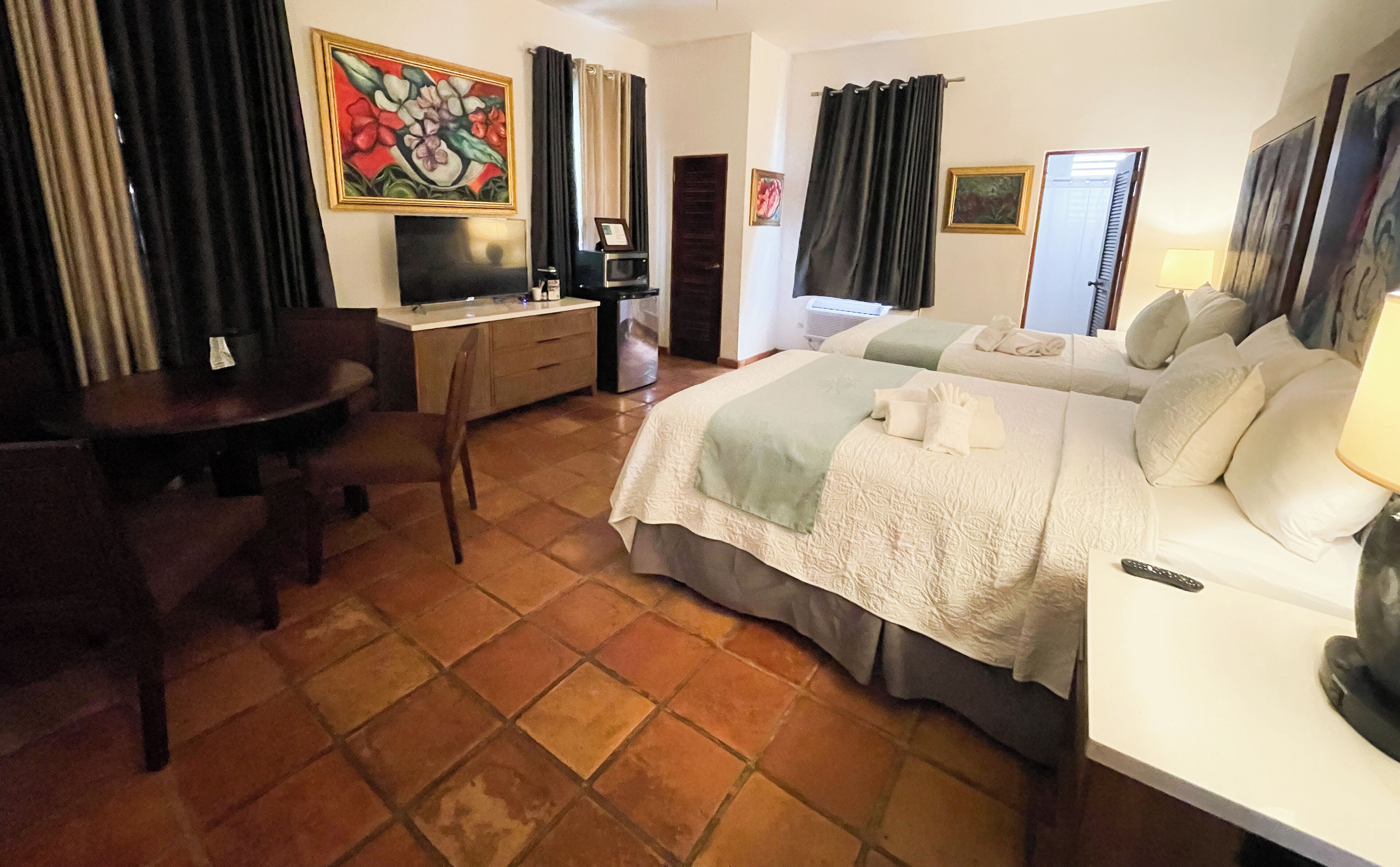 Habitación de hotel con cama, escritorio, silla, televisor y un cuadro en la pared.