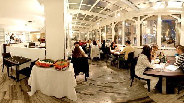 A restaurant with a high ceiling and large windows, marble flooring, and tables set for dining. - Hotel Ambassador Monaco (Monaco)