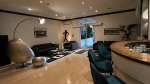A modern living room with a wooden floor, a large abstract sculpture, and a dining area with teal chairs and a marble countertop. - Hotel Ambassador Monaco (Monaco)