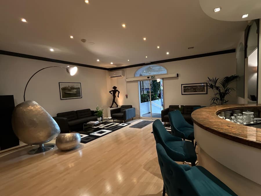 Una sala moderna con piso de madera, una gran escultura abstracta, y un comedor con sillas color turquesa y encimera de mármol.