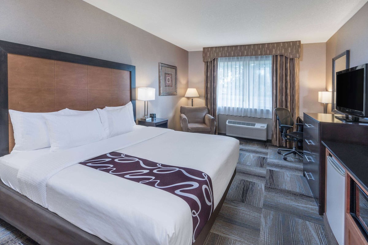 A hotel room with a large bed, a desk with a television, a chair, a desk lamp, and a window with curtains.