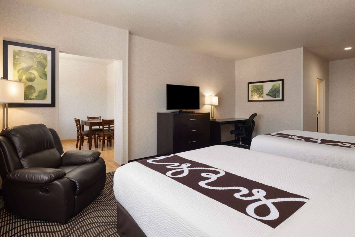 A hotel room with a large bed, a leather chair, a desk with a chair, a television, and artwork on the walls.