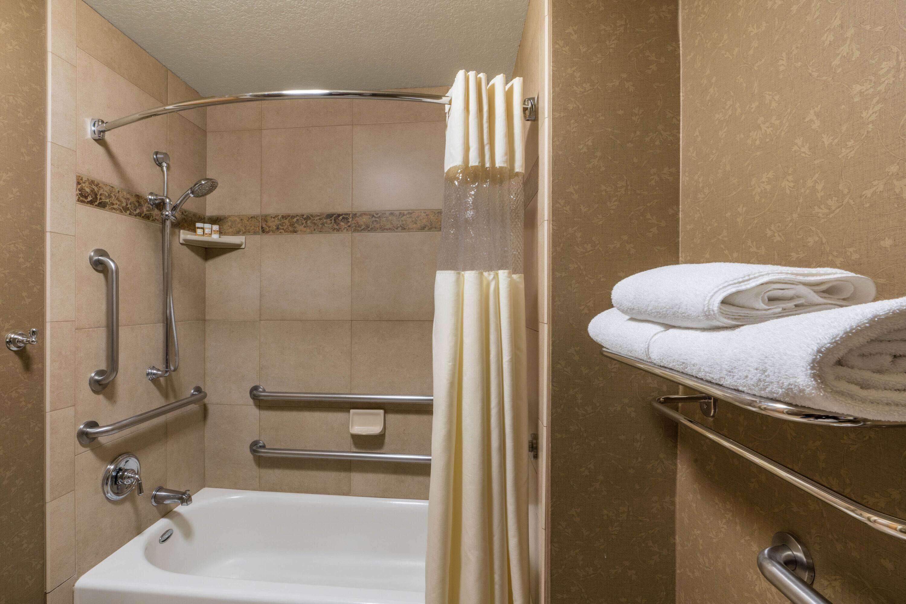 A bathroom with a bathtub, grab bars, a shower with a curtain, and a towel rack with folded towels.