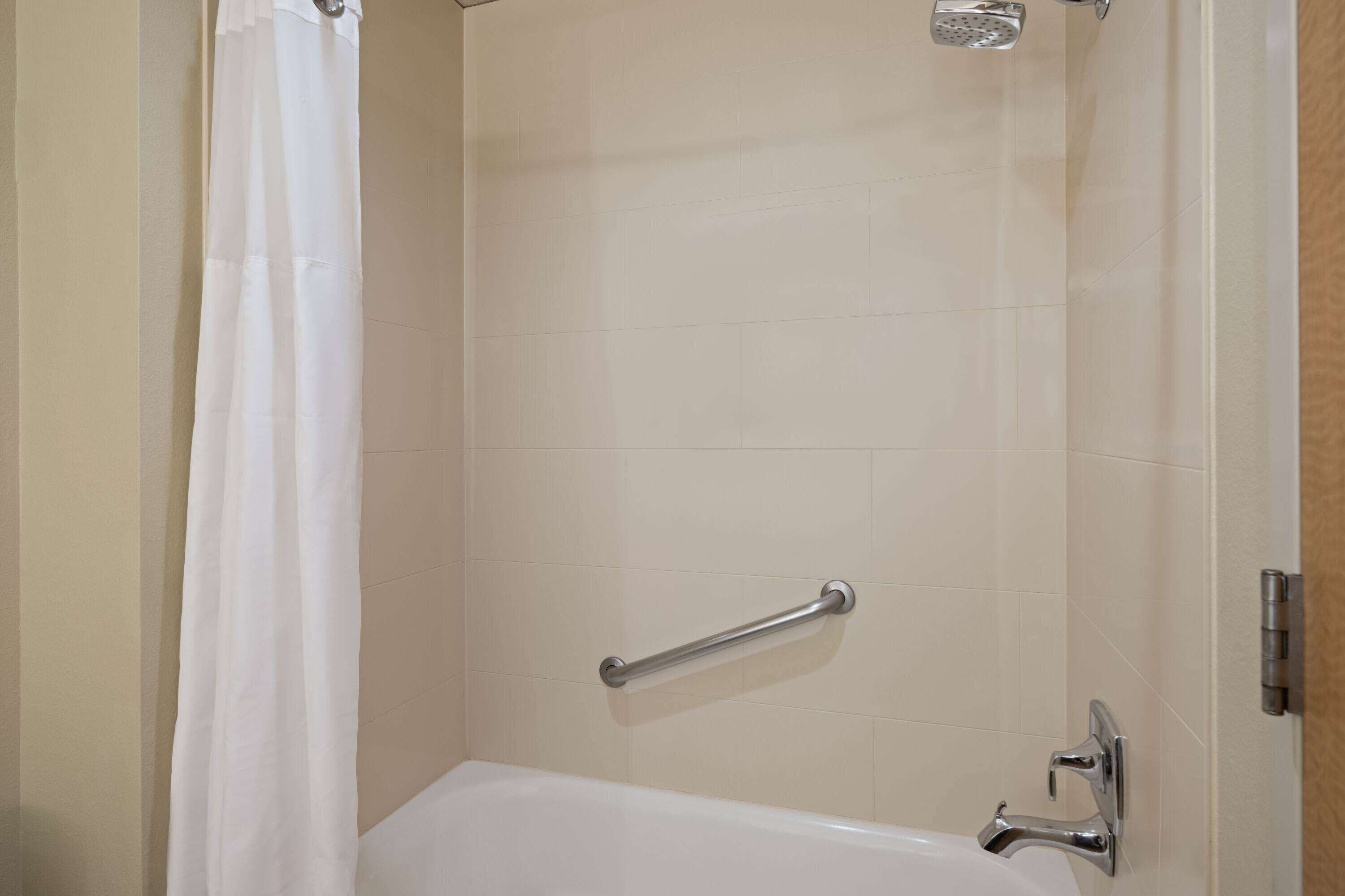 A bathroom with a bathtub, a shower curtain, and a grab bar.