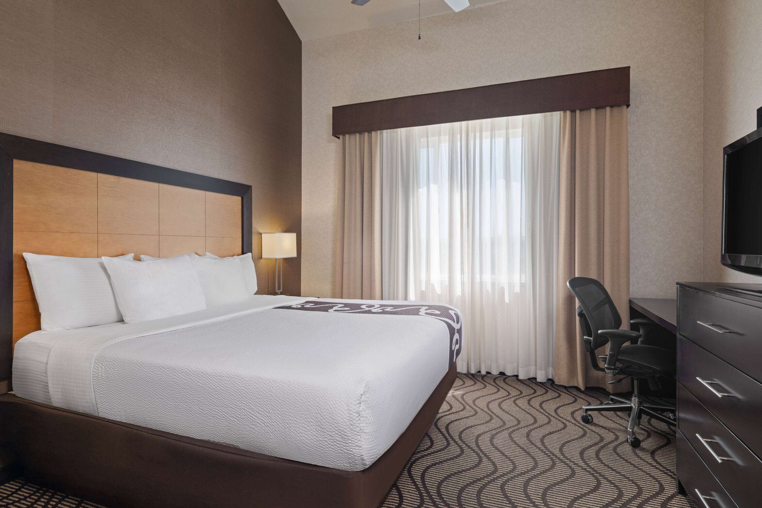 Habitación de hotel con una cama grande, un escritorio con silla, una cómoda y un televisor.