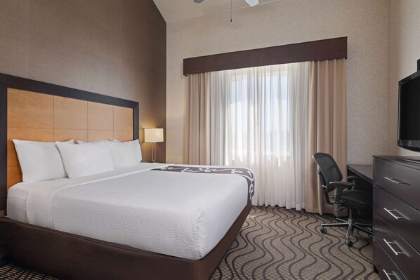 Habitación de hotel con una cama grande, un escritorio con silla, una cómoda y un televisor.