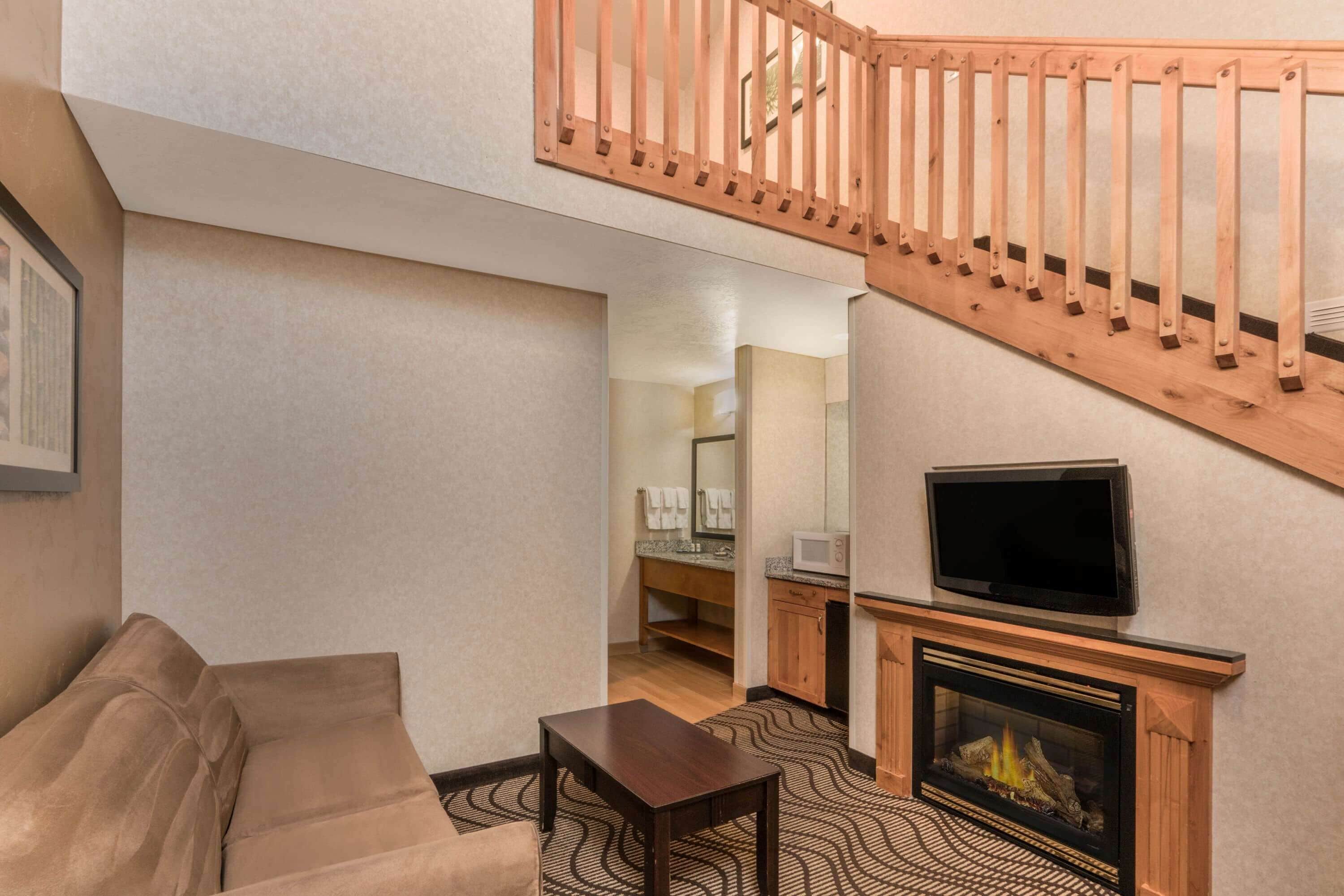 A living room with a sofa, a coffee table, a fireplace, a TV, and a wooden staircase.