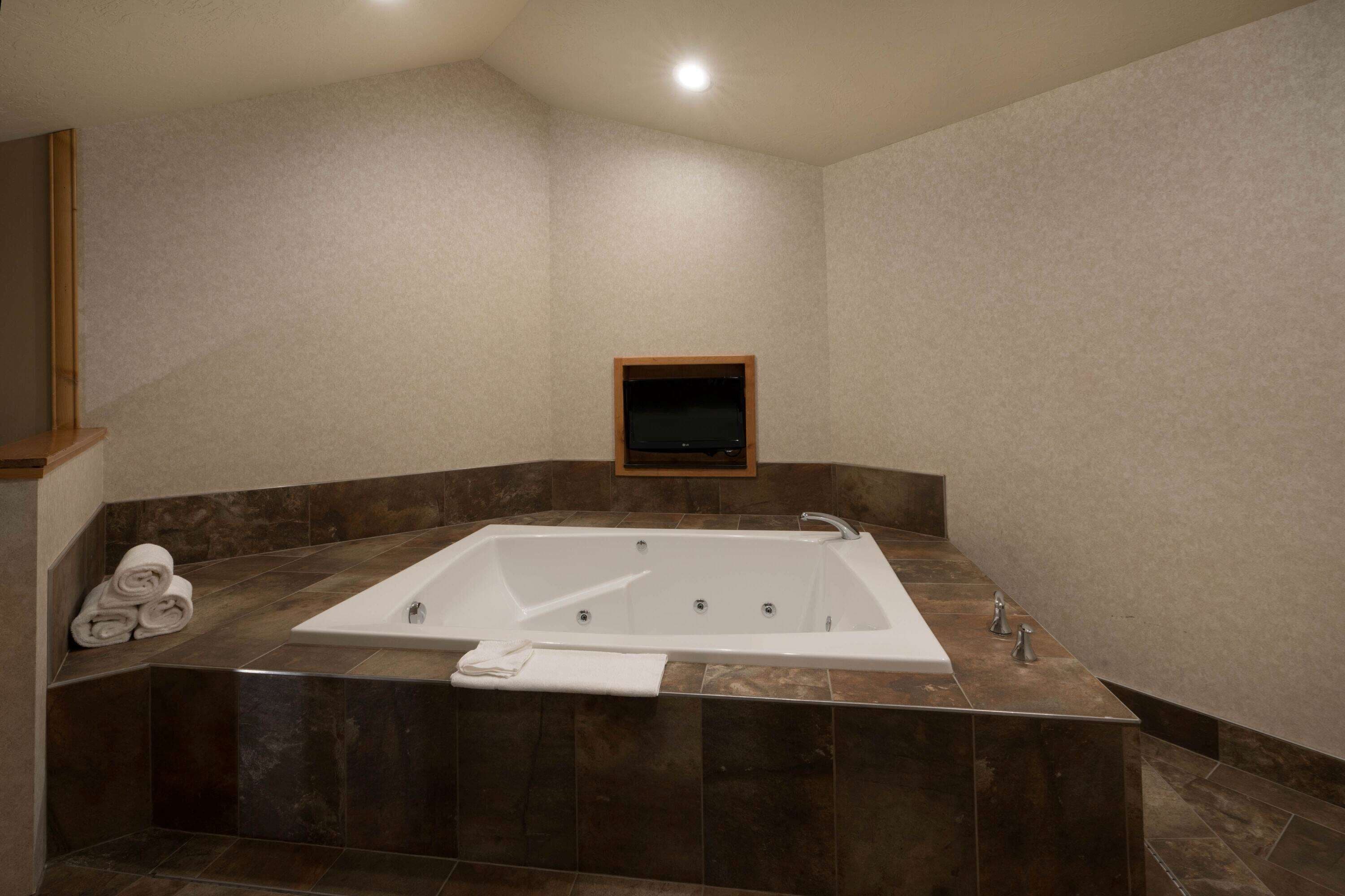 A modern bathroom with a large freestanding bathtub, a small framed mirror, and neatly folded towels on a shelf.