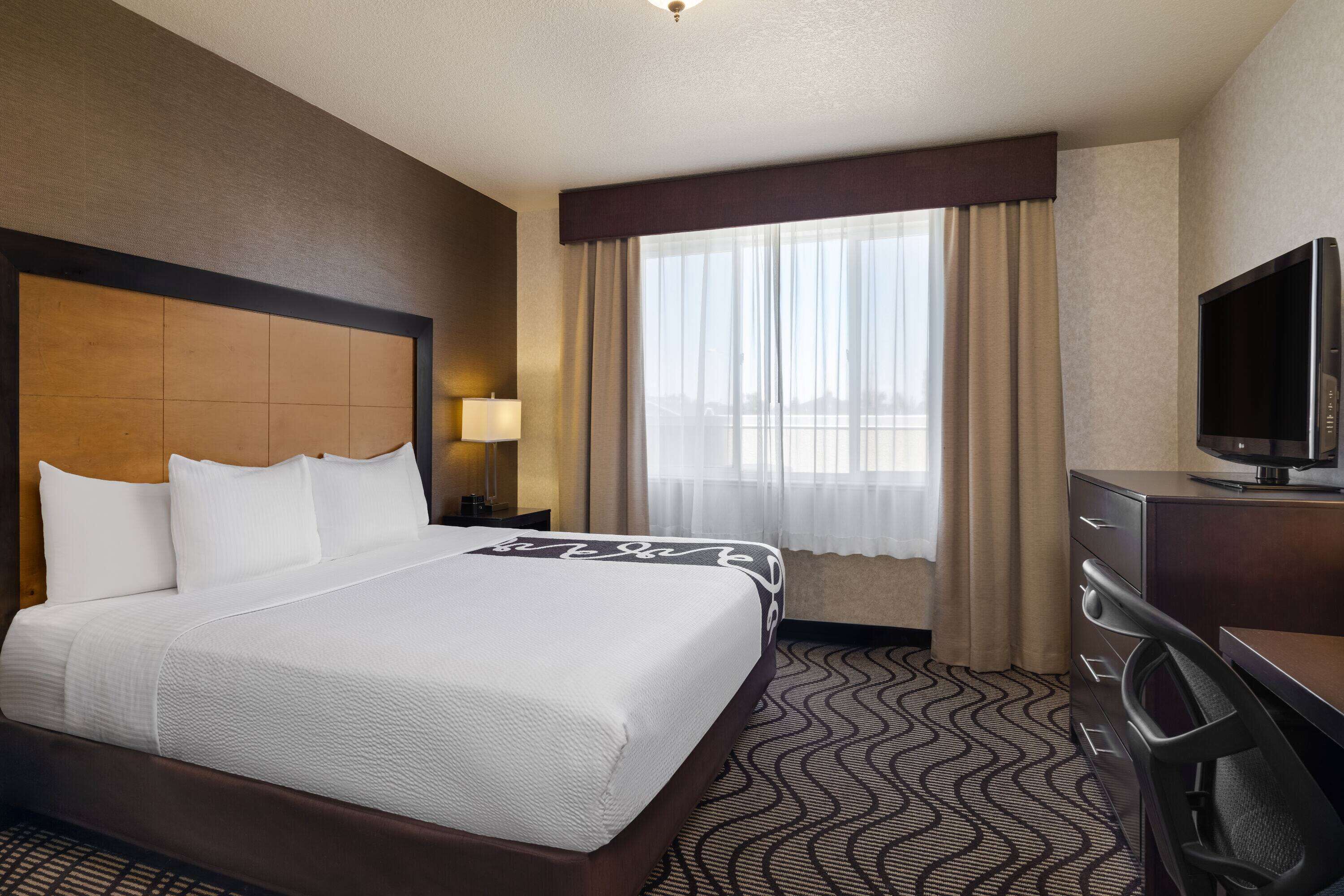 Habitación de hotel con una cama grande, televisor, escritorio y ventana con cortinas.