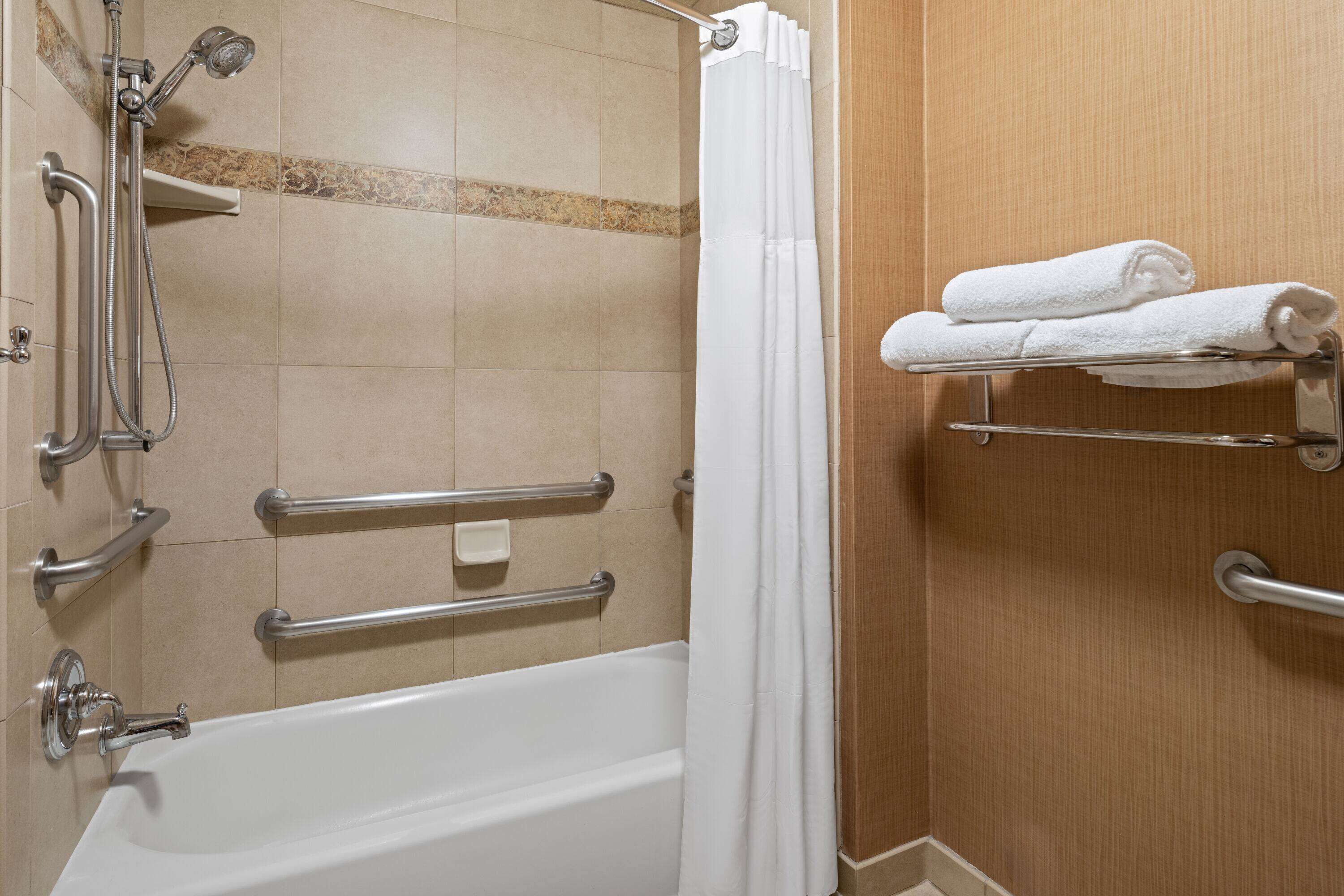 Un baño con bañera, ducha y barras de apoyo.