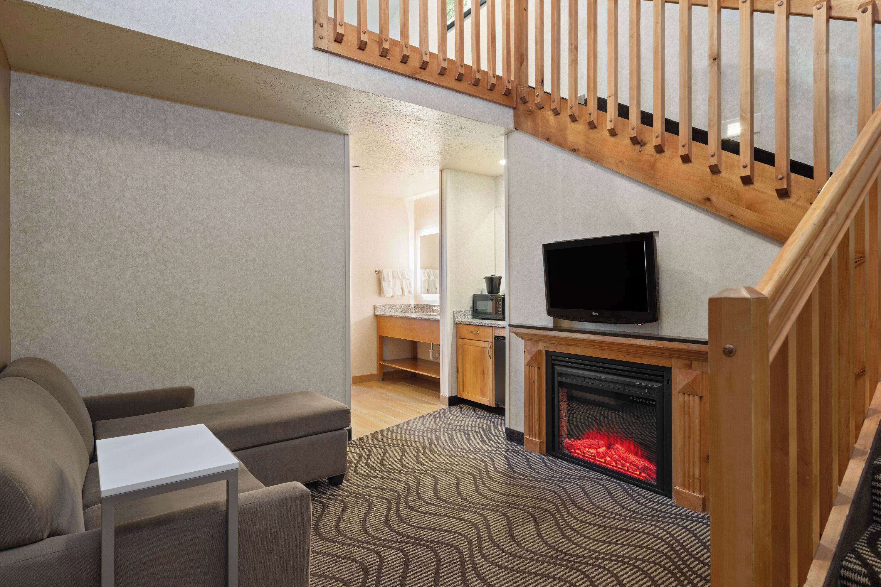 A modern living room with a fireplace, a television, and a staircase.