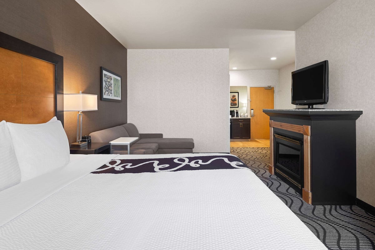 A hotel room with a large bed, a sofa, a TV, and a fireplace.