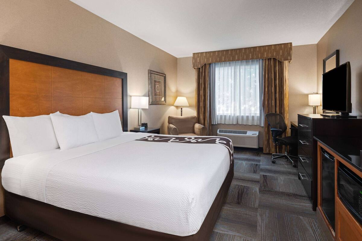 A hotel room with a large bed, a desk with a television, a chair, and a window with curtains.