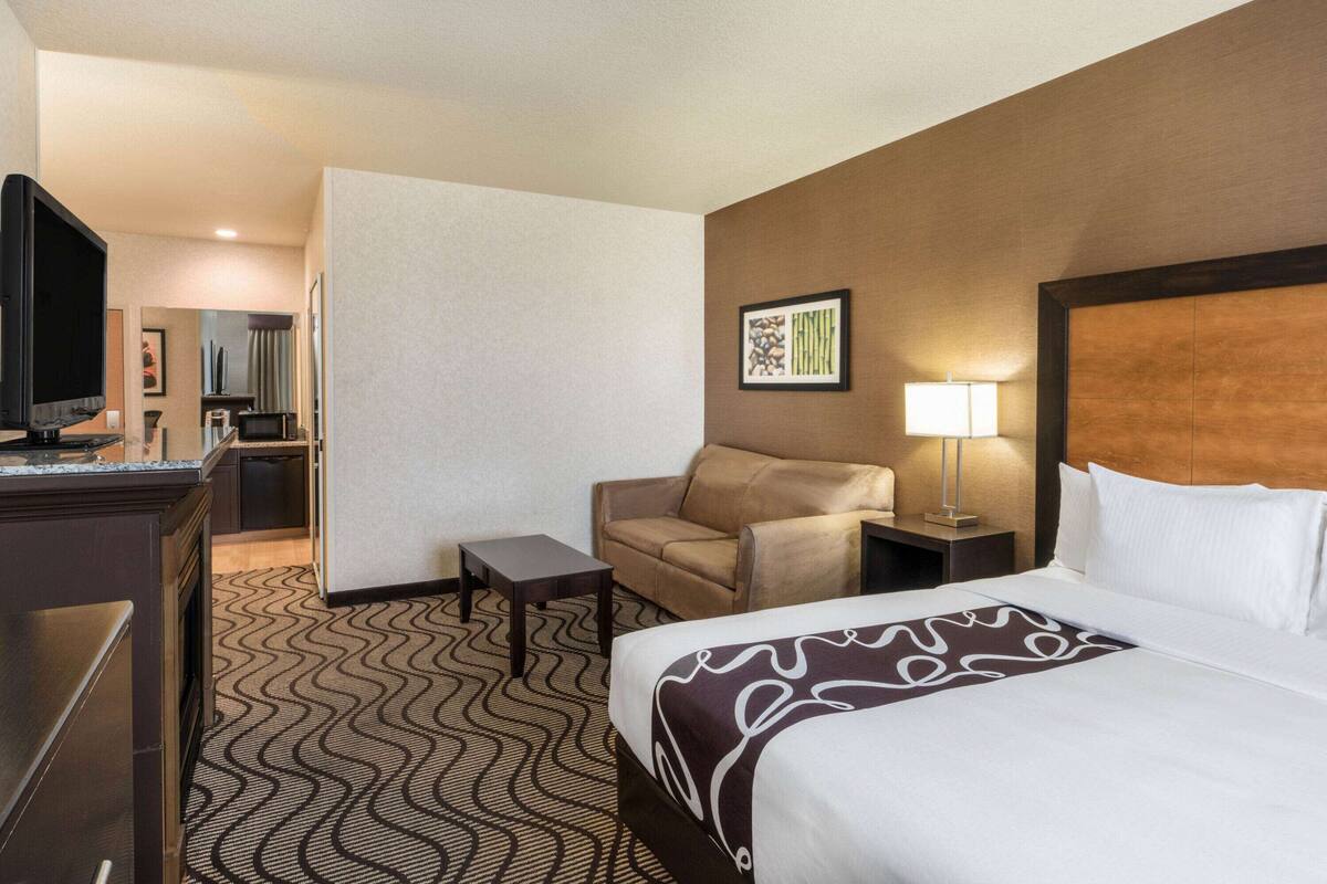 A hotel room with a bed, a desk, a chair, a TV, and a microwave.