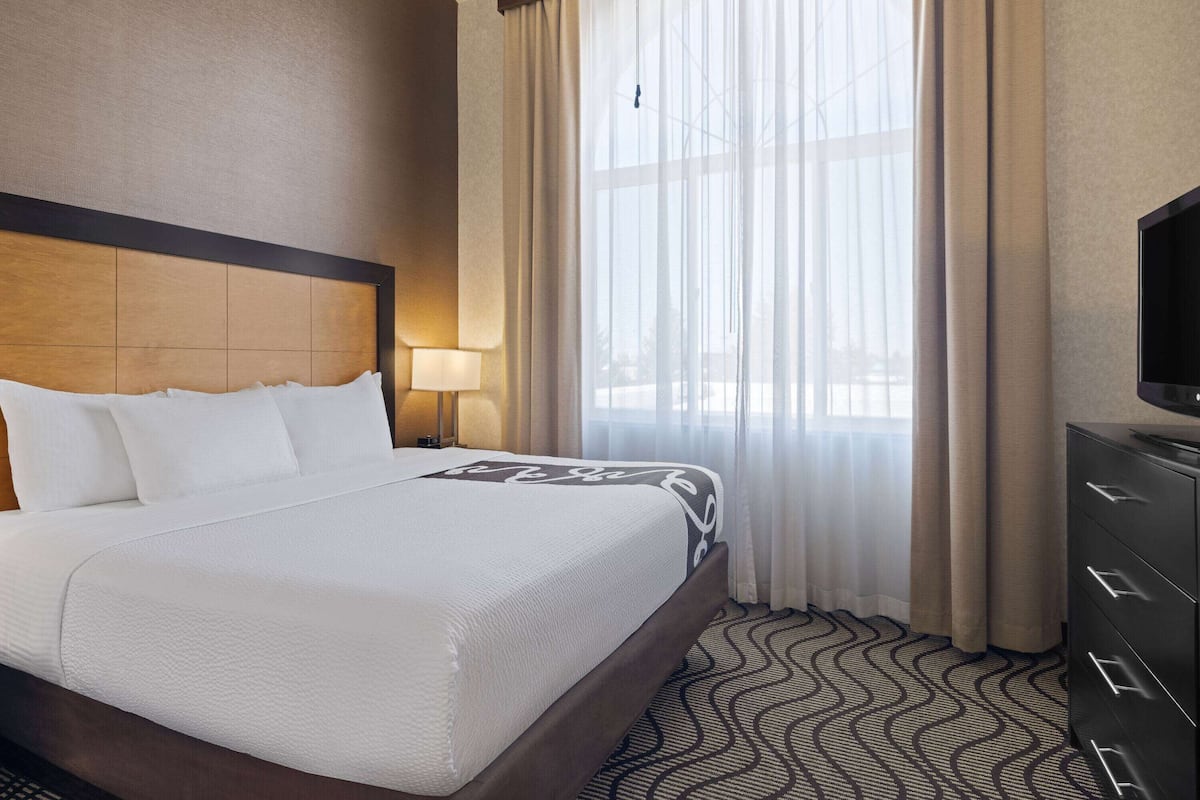 A hotel room with a large bed, a TV, a nightstand, and a window with sheer curtains.