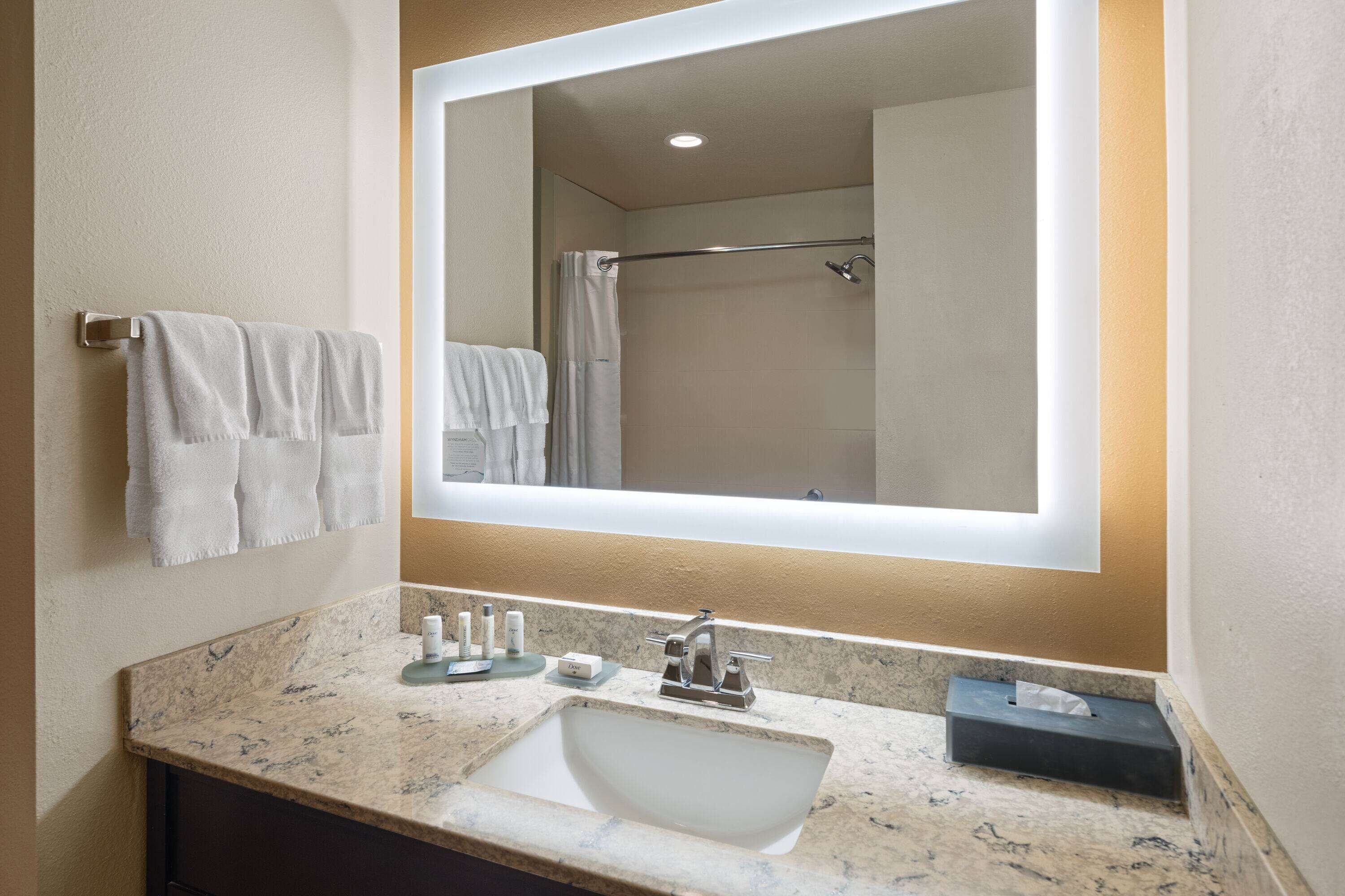 A bathroom with a marble sink, a large mirror, and two towels hanging on the wall.
