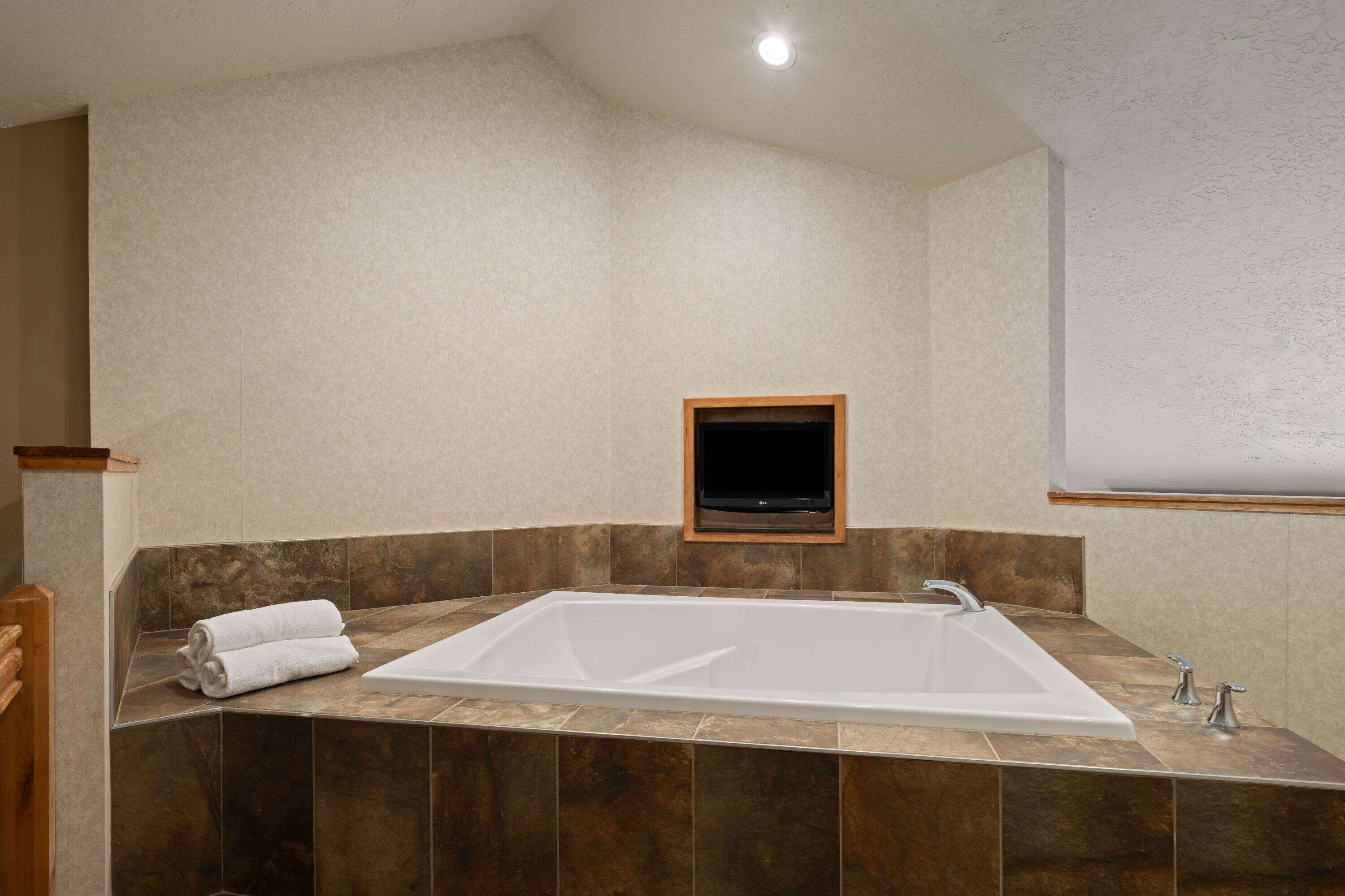 Un bagno moderno con una vasca da bagno ampia, un televisore con cornice in legno e un asciugamano sul pavimento.