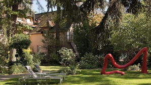 A garden with a red sculpture, a white bench, and a house in the background. - CAZAUDEHORE Hôtel Restaurant Gastronomique Terrasse et Jardins (Saint-Germain-en-Laye)